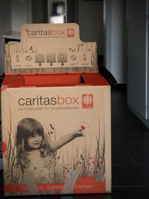 Nachhaltigkeit mit der CaritasBox. Das Sammelsystem für gebrauchte Druckerpatronen steht hier im Flur von TEXT_SITE Übersetzungen.